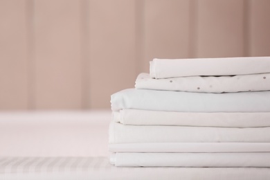 Photo of Stack of clean folded linens on bed indoors. Space for text