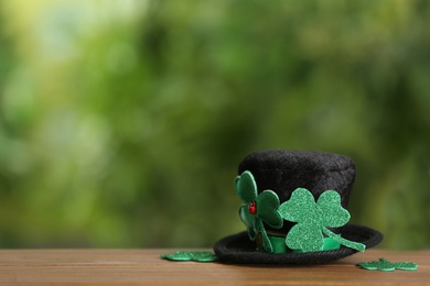 Leprechaun hat and clover leaves on wooden table against blurred background, space for text. St Patrick's Day celebration