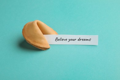 Image of Tasty fortune cookie with prediction Believe your dreams on cyan background