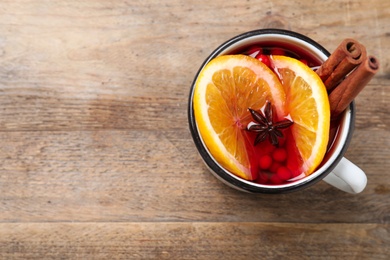 Photo of Mug with aromatic mulled wine on wooden table, top view. Space for text