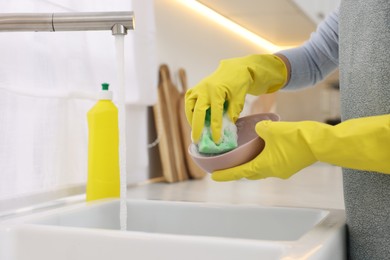 Woman washing plate above sink in modern kitchen, closeup