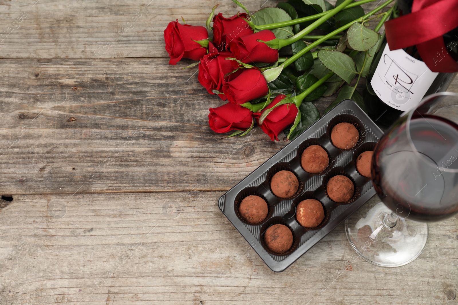 Photo of Red wine, chocolate truffles and roses on wooden table, flat lay. Space for text