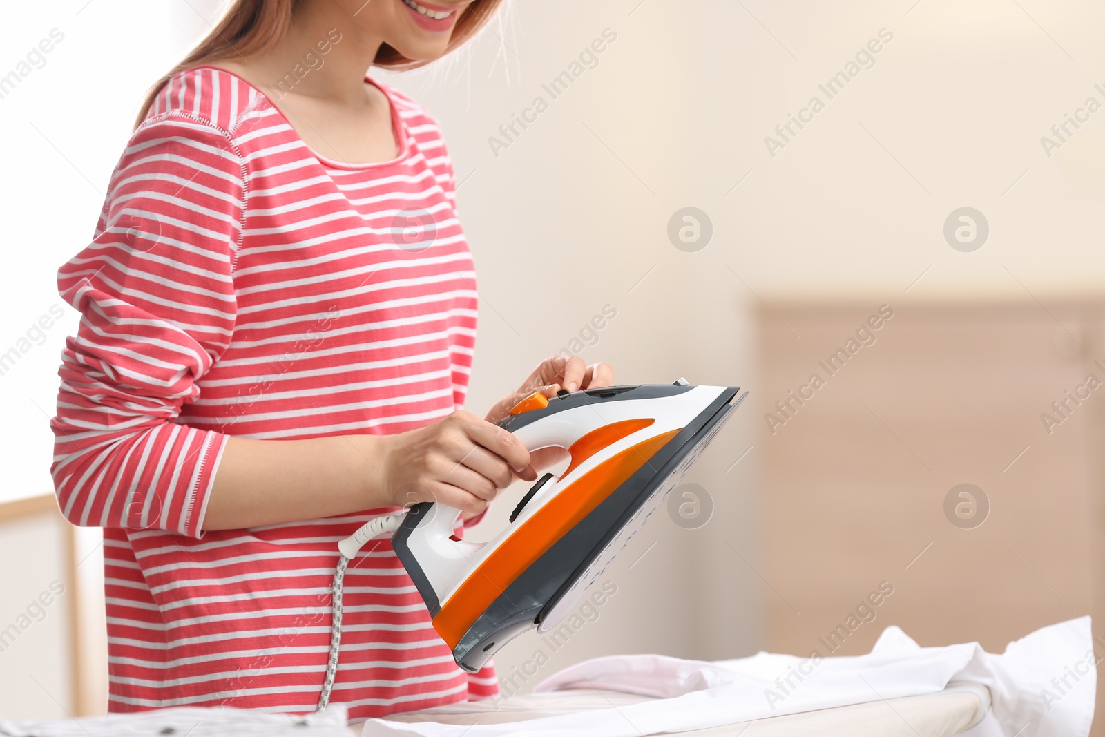 Photo of Young woman ironing clean laundry on board indoors, closeup