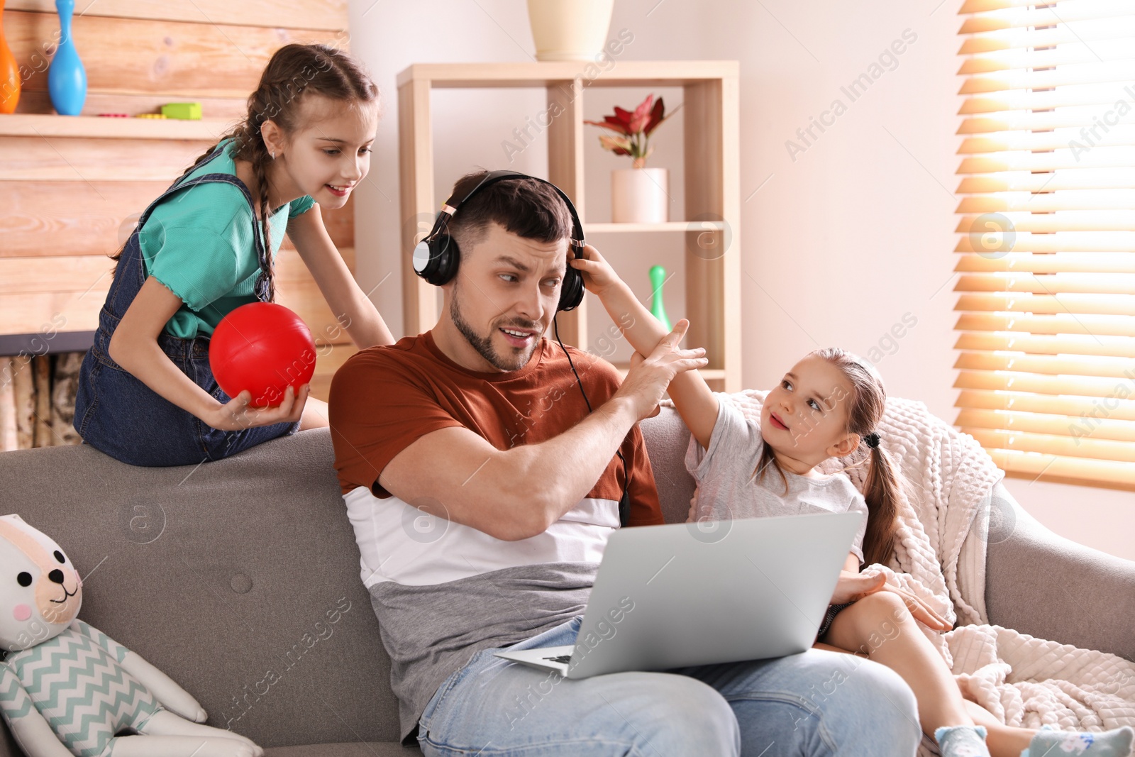 Photo of Children disturbing stressed man in living room. Working from home during quarantine