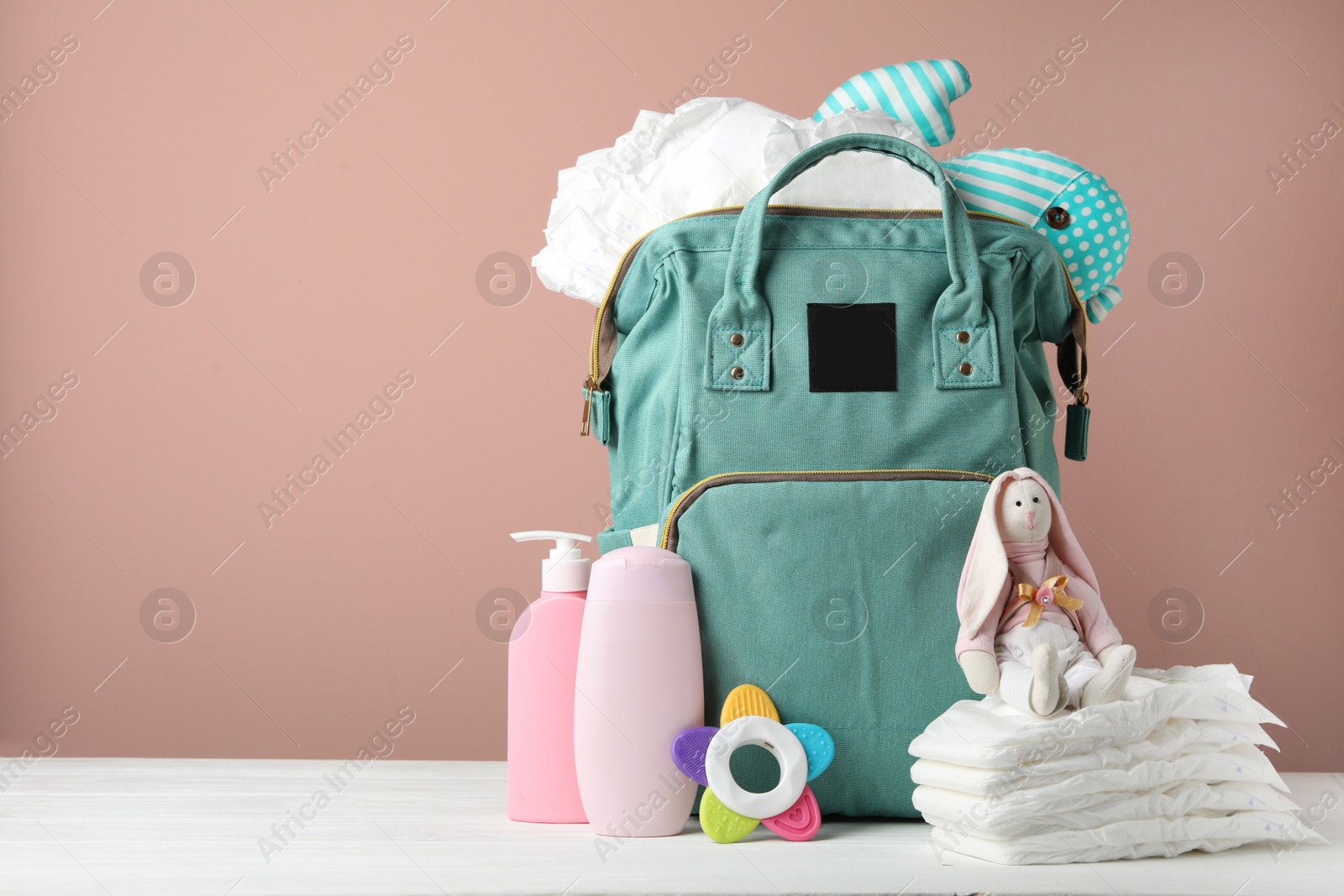 Photo of Bag with diapers and baby accessories on white wooden table against pink background. Space for text