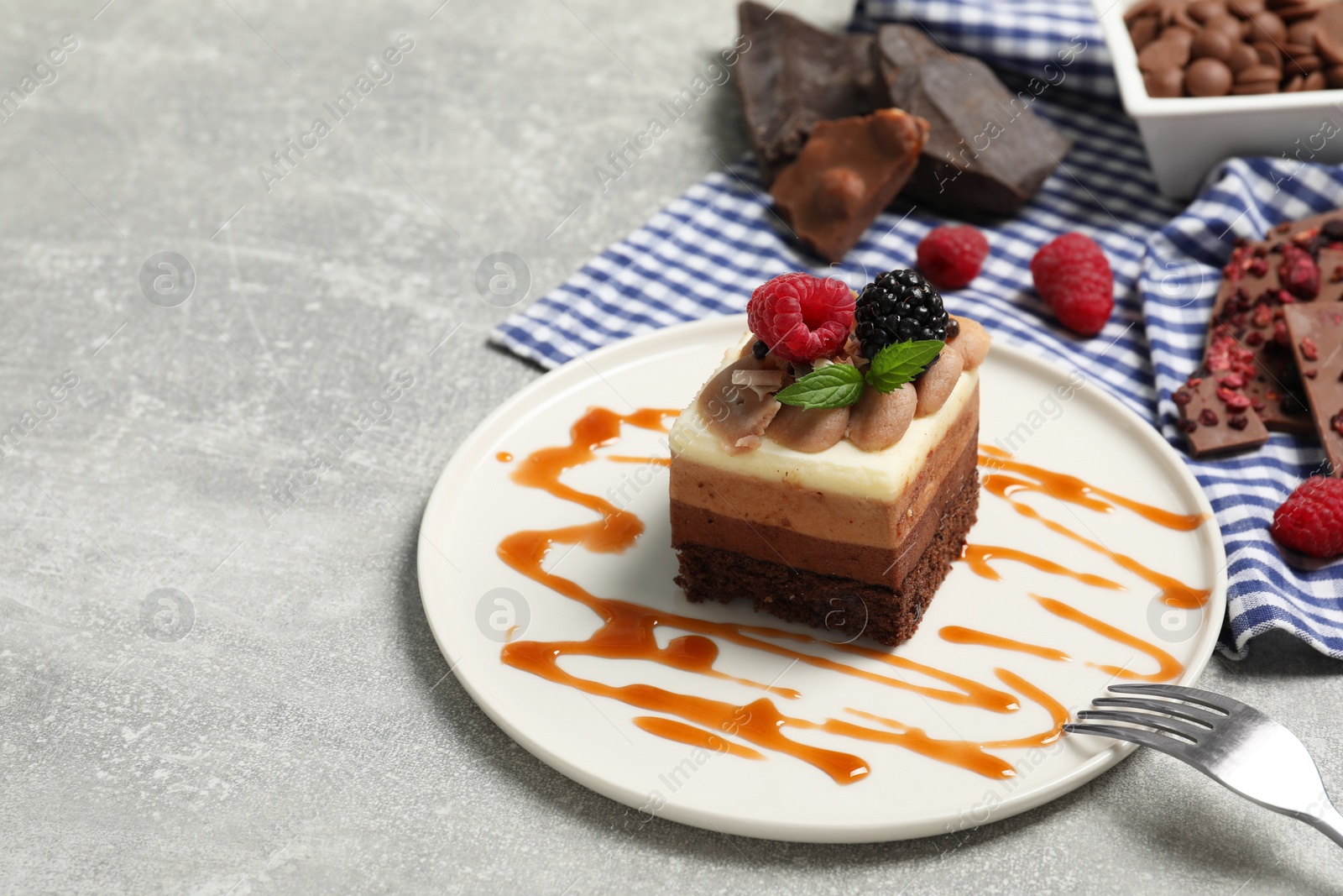 Photo of Piece of triple chocolate mousse cake with fresh berries served on light grey table, closeup. Space for text