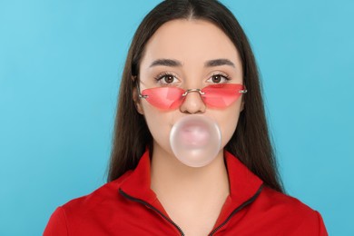 Photo of Beautiful young woman blowing bubble gum on light blue background