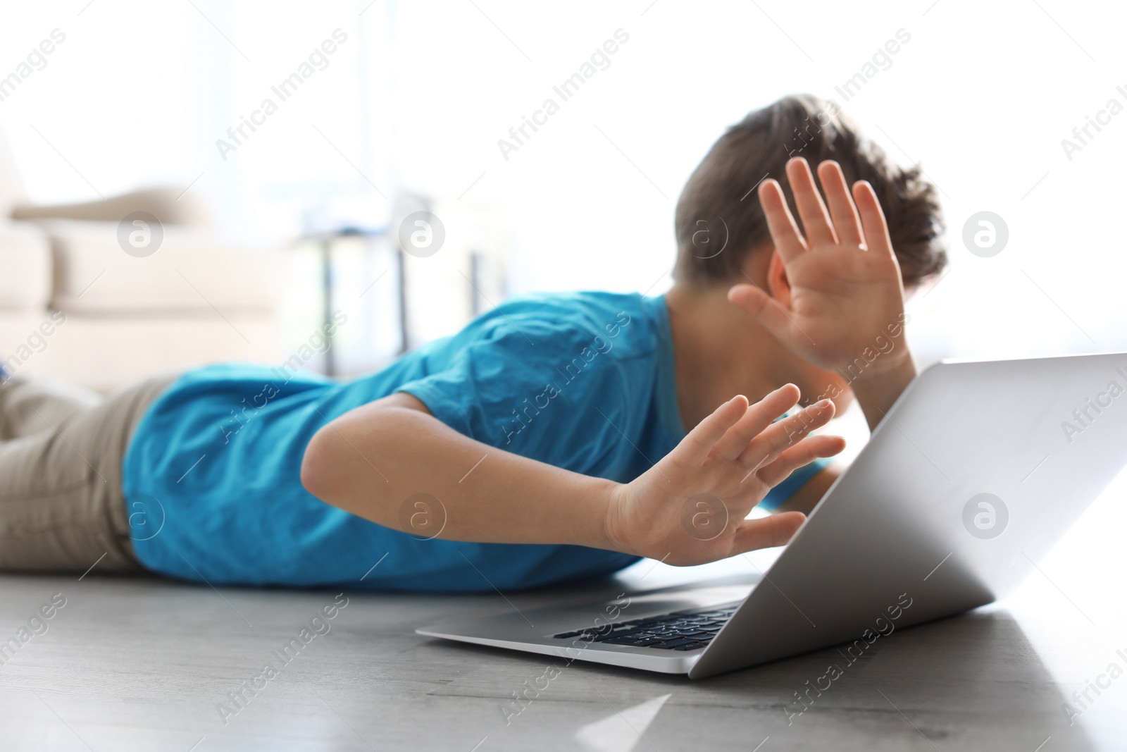 Photo of Frightened little child with laptop on floor indoors. Danger of internet