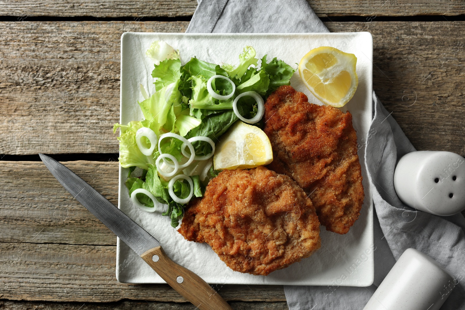 Photo of Tasty schnitzels served with lemon and salad on wooden table, flat lay