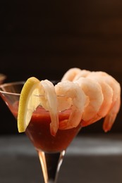 Tasty shrimp cocktail with sauce in glass and lemon on table, closeup