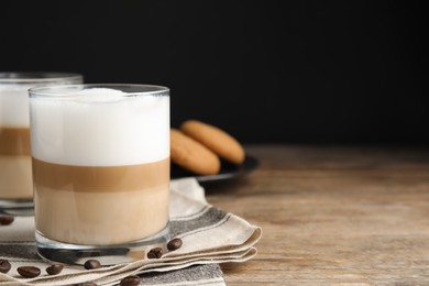 Photo of Delicious latte macchiato and coffee beans on wooden table, space for text