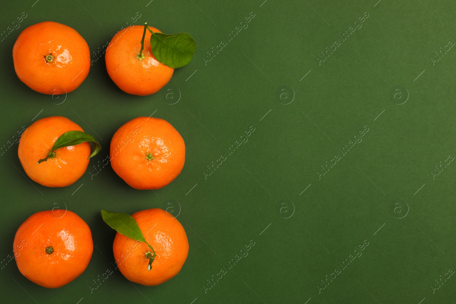 Photo of Delicious tangerines and leaves on green background, flat lay. Space for text