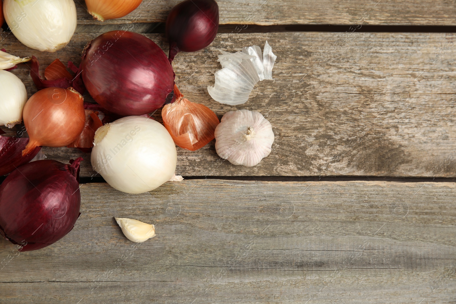 Photo of Fresh onion bulbs and garlic on wooden table, flat lay. Space for text