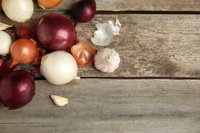 Fresh onion bulbs and garlic on wooden table, flat lay. Space for text