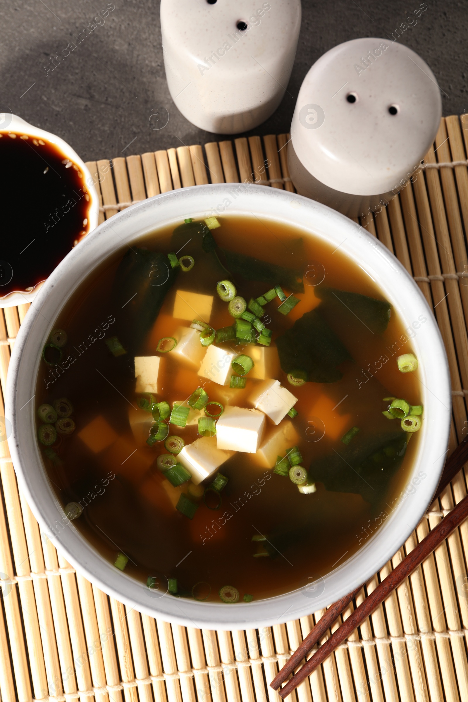Photo of Bowl of delicious miso soup with tofu served on grey table, flat lay