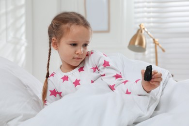 Photo of Sad little girl finding piece of coal under pillow in bed at home. Saint Nicholas day tradition