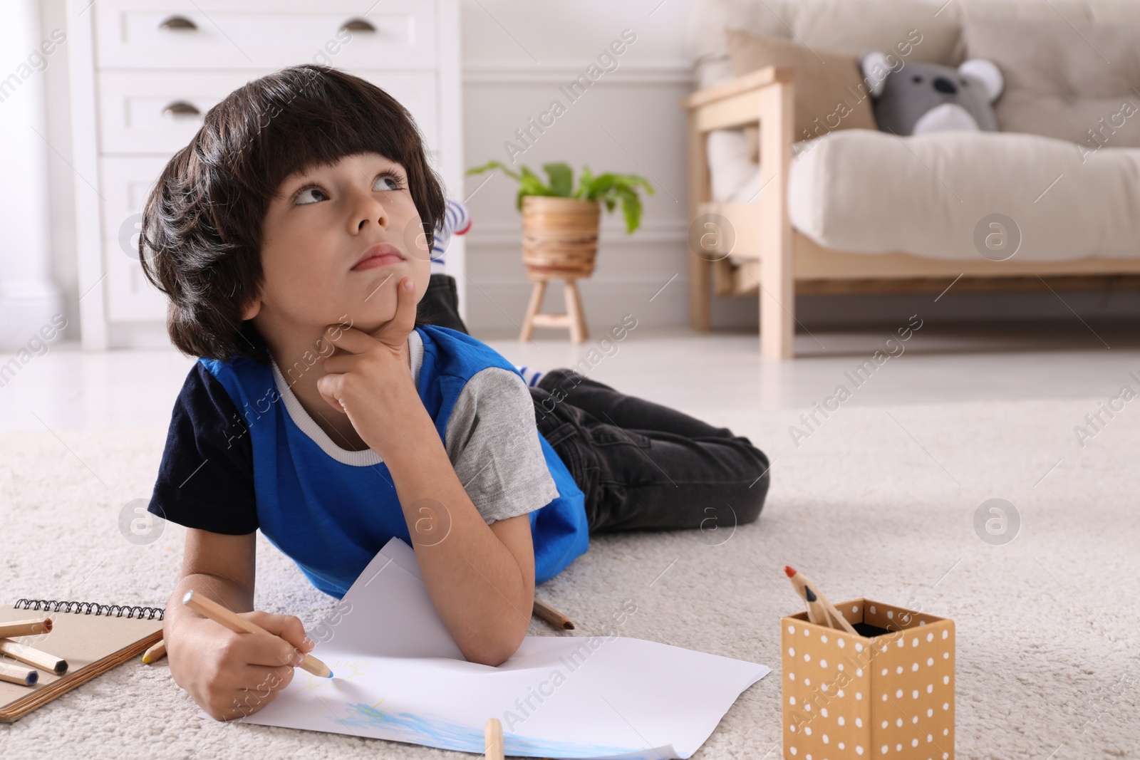 Photo of Cute little boy drawing with pencils on floor at home