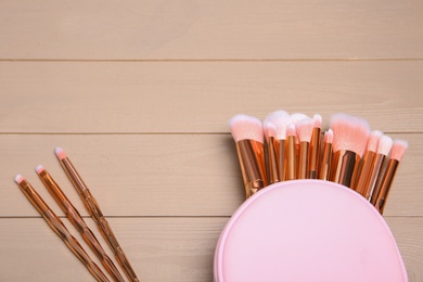 Set of professional makeup brushes with bag on wooden background, above view. Space for text