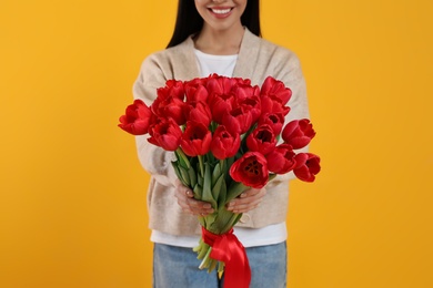 Happy woman with red tulip bouquet on yellow background, closeup. 8th of March celebration