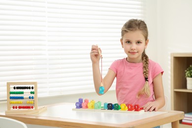 Photo of Little girl playing with Educational game Fishing for Numbers at desk in room. Learning mathematics with fun