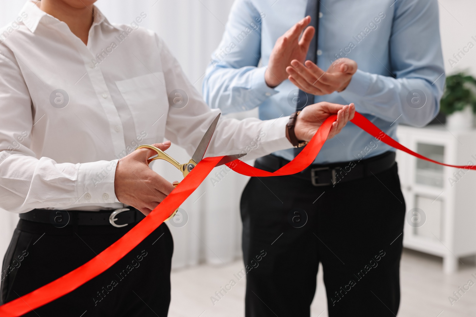 Photo of Woman cutting red ribbon with scissors indoors, closeup