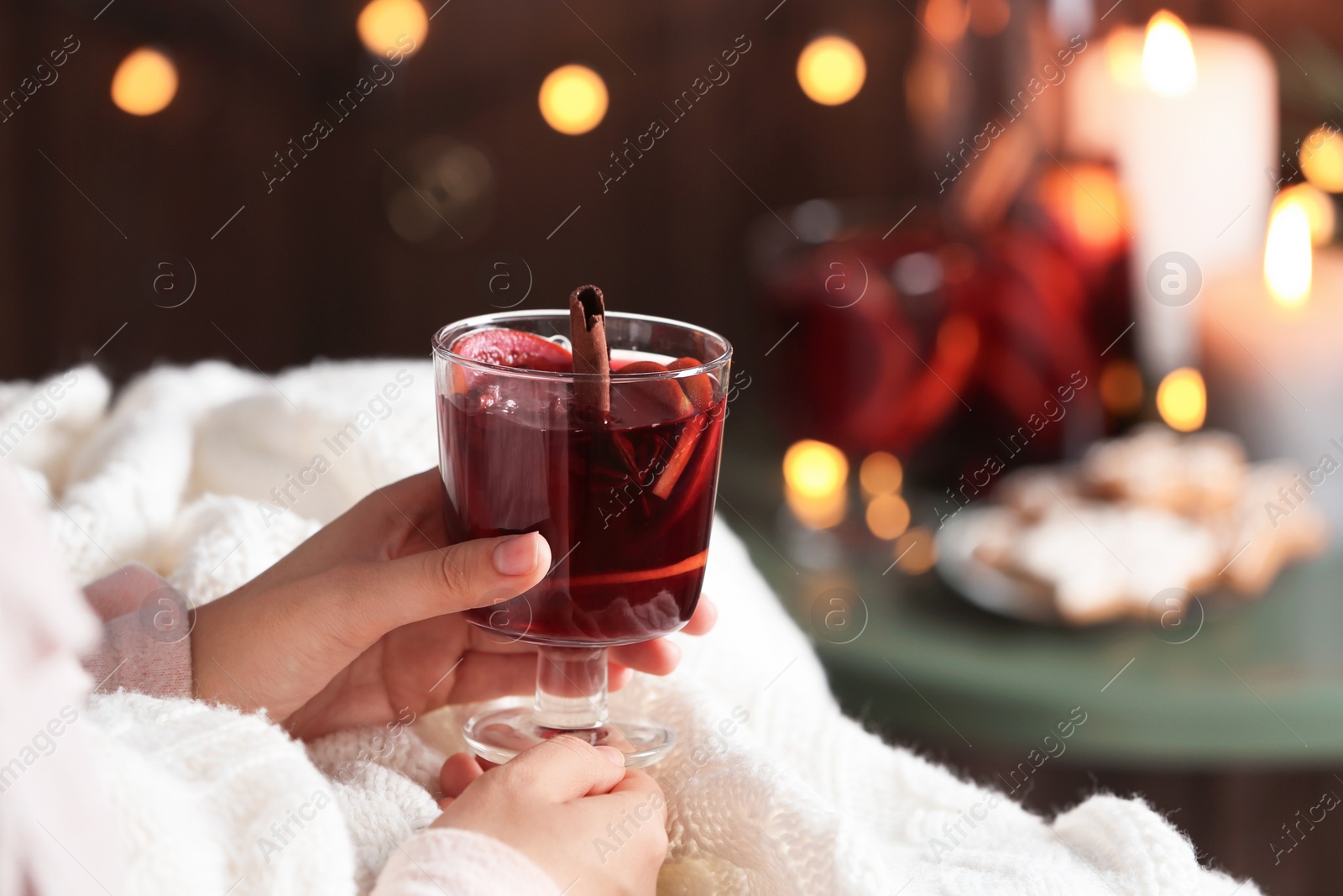 Photo of Woman with glass of mulled wine at home, focus on hands. Space for text