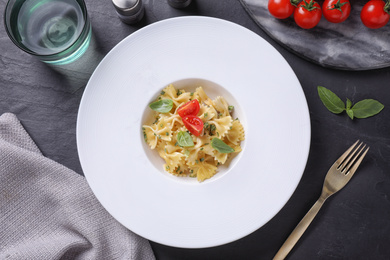 Photo of Delicious pasta with tomatoes and basil served on black table, flat lay