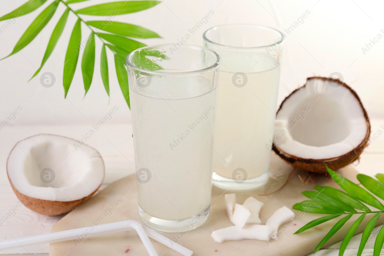 Photo of Glasses of coconut water, palm leaves and nuts on white table