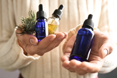 Woman holding bottles of essential oils and fir branches, closeup