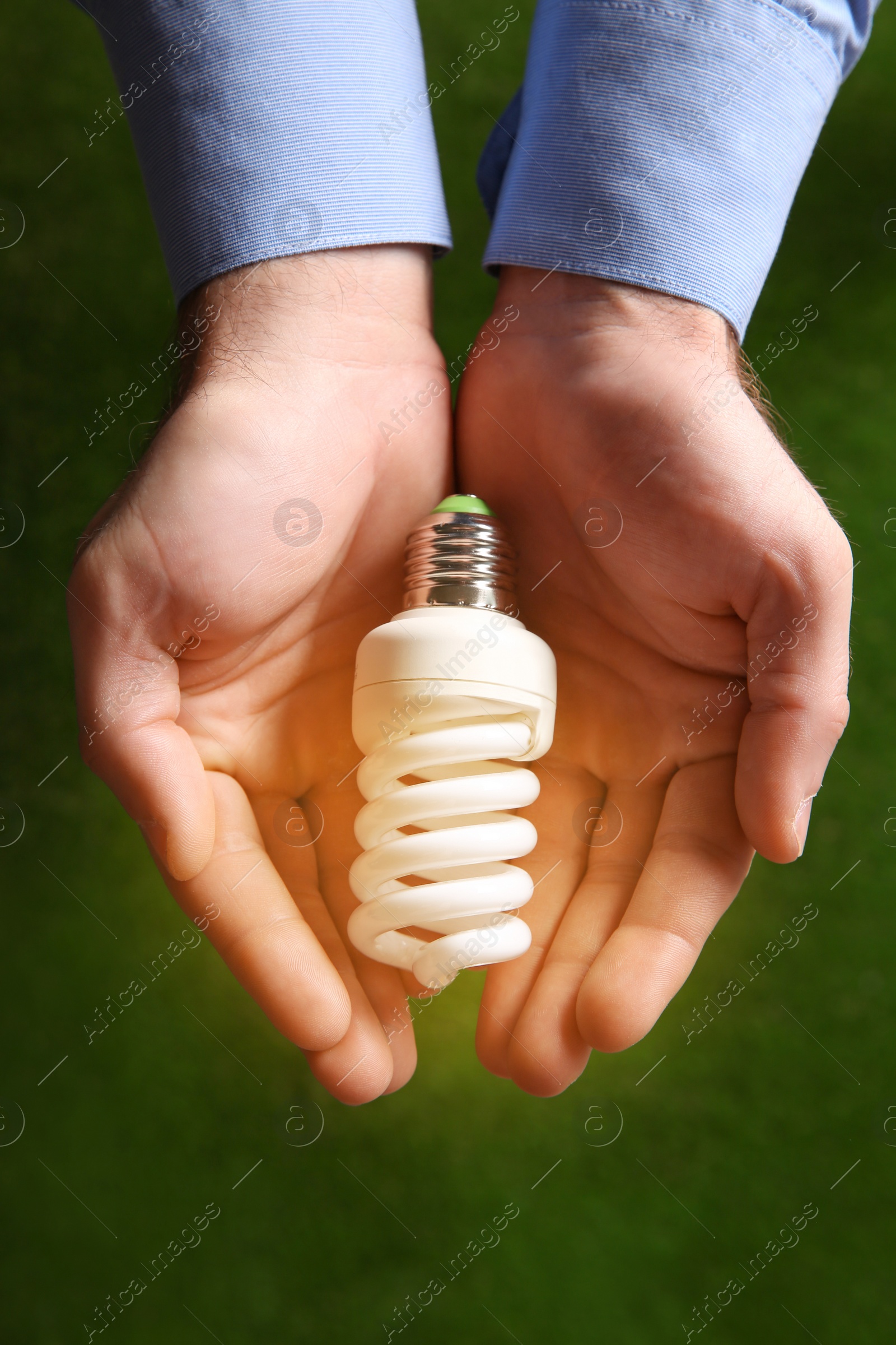 Photo of Man holding energy saving bulb for lamp on green background, top view