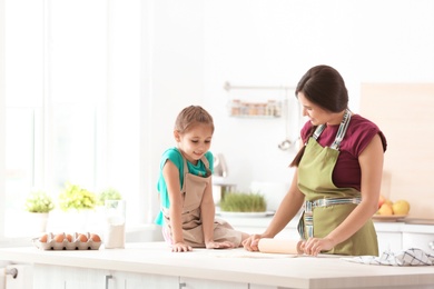 Mother and her daughter preparing dough at table in kitchen