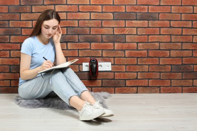 Photo of Woman sitting on floor while charging electric heater indoors, space for text