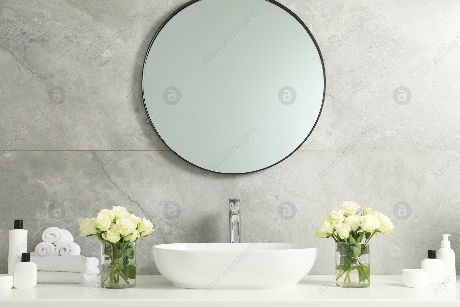 Photo of Beautiful roses, bath accessories, sink and mirror in bathroom