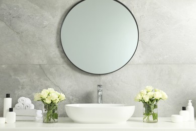 Beautiful roses, bath accessories, sink and mirror in bathroom