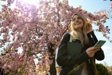 Photo of Happy woman with smartphone listening to audiobook outdoors on spring day