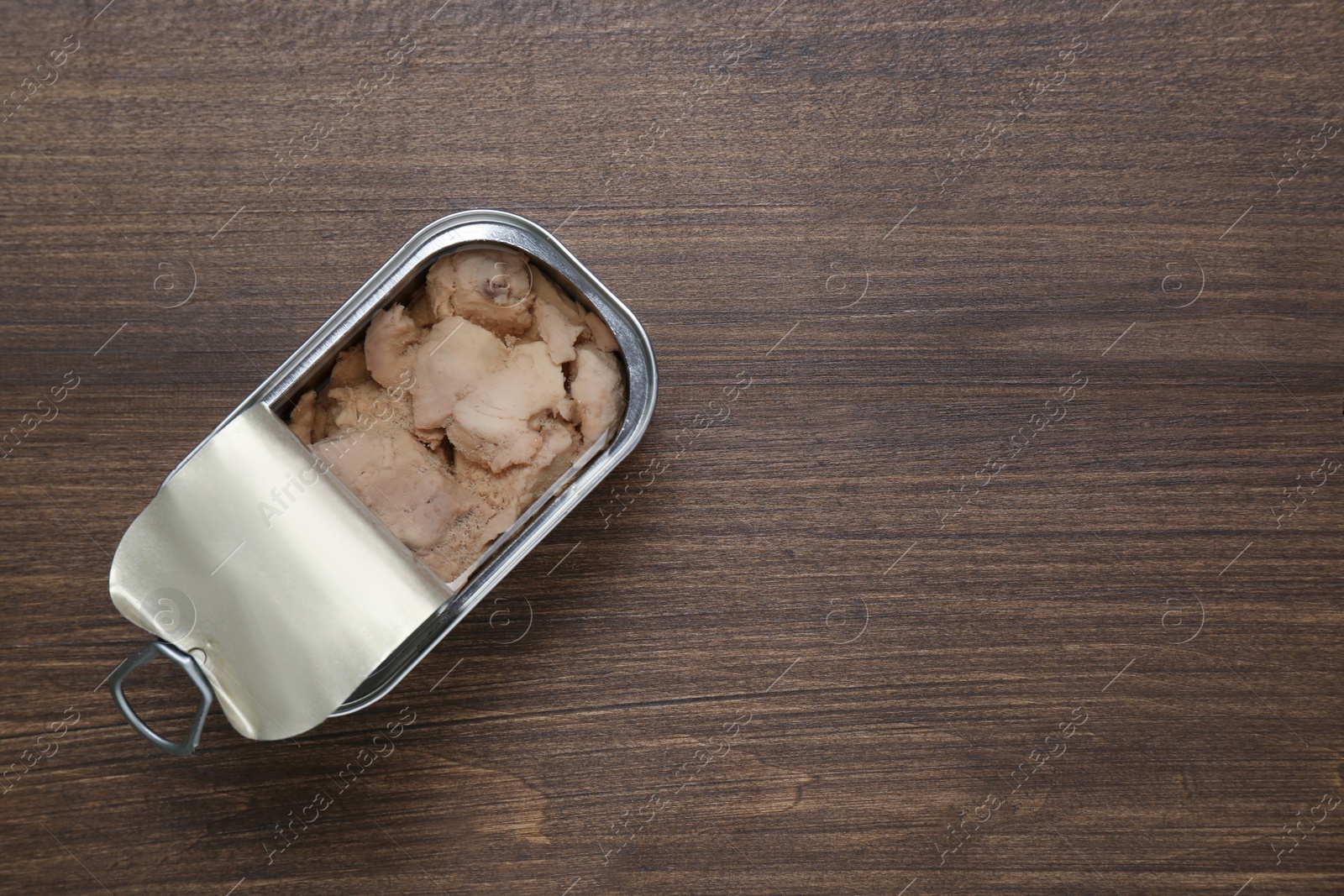 Photo of Open tin can of tasty cod liver on wooden table, top view. Space for text