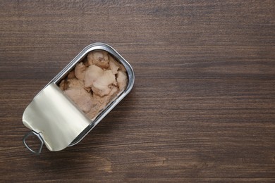Open tin can of tasty cod liver on wooden table, top view. Space for text