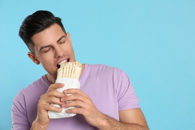 Photo of Man eating delicious shawarma on turquoise background, space for text