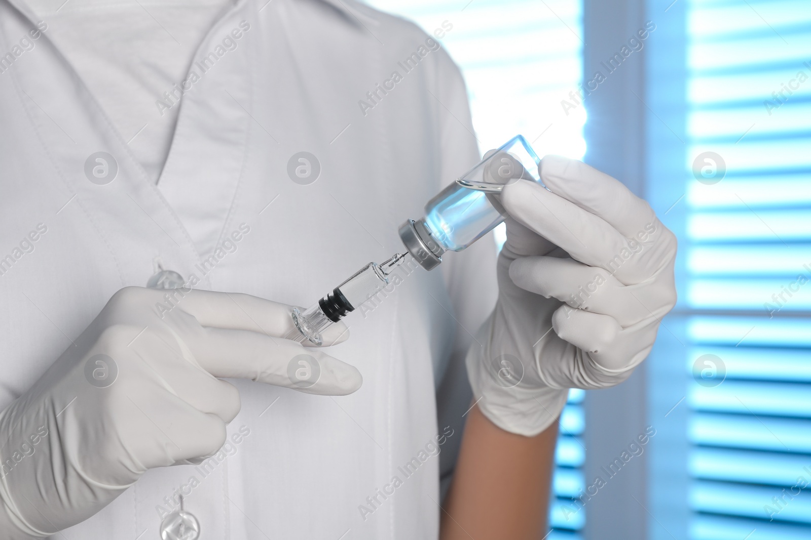 Photo of Doctor filling syringe with vaccine from vial indoors, closeup