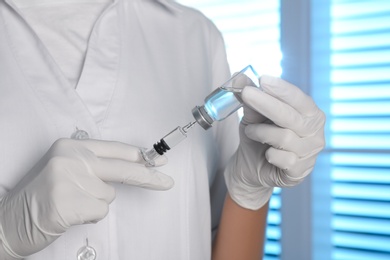 Photo of Doctor filling syringe with vaccine from vial indoors, closeup