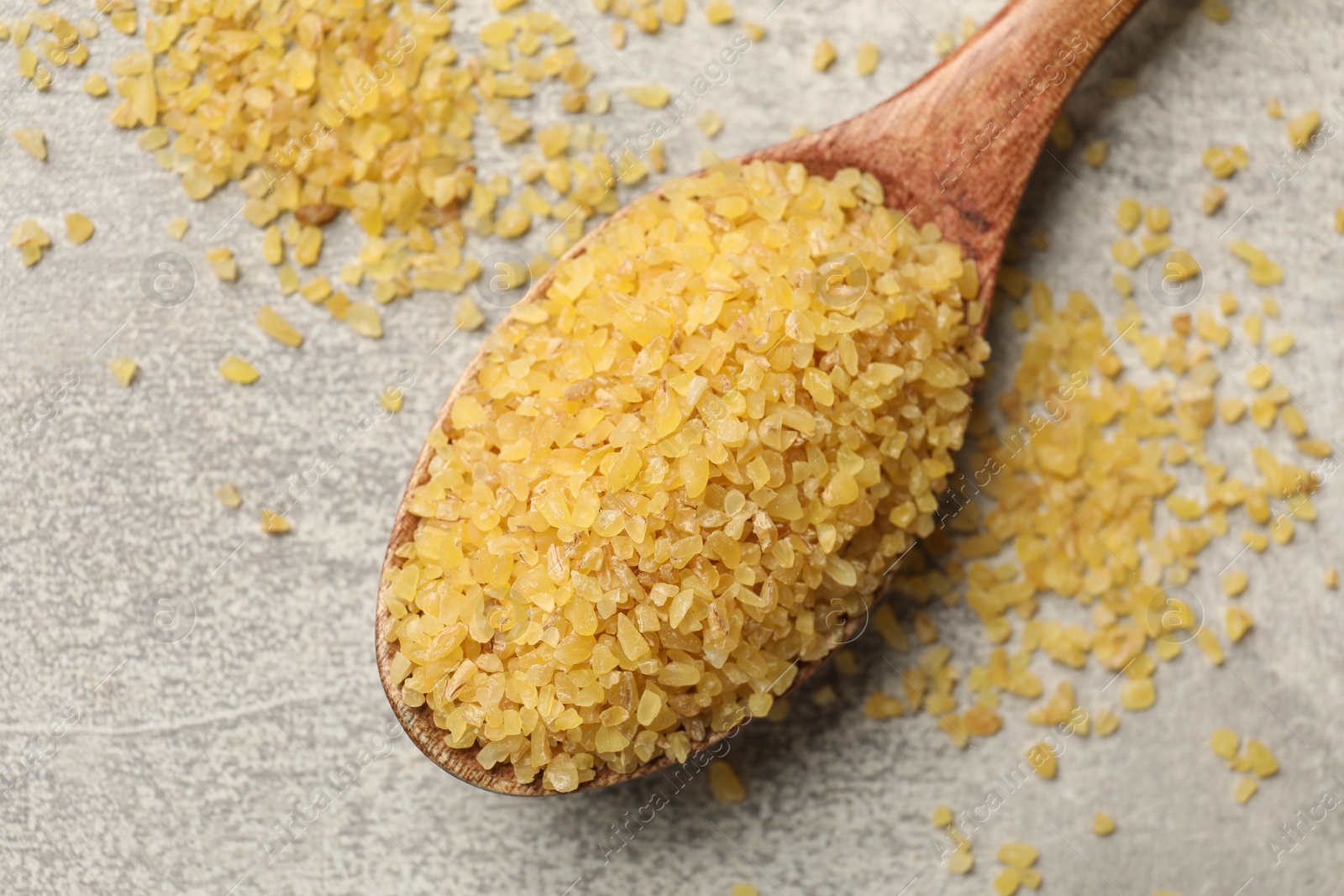 Photo of Spoon with raw bulgur on gray table, closeup