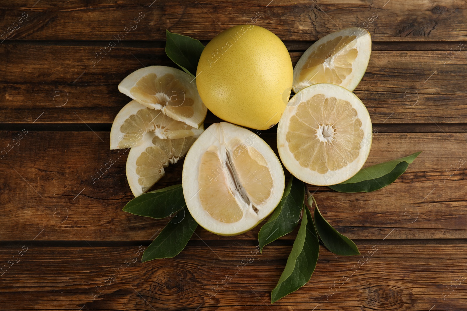 Photo of Fresh cut and whole pomelo fruits with leaves on wooden table, flat lay