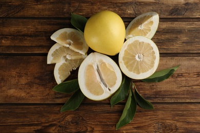 Photo of Fresh cut and whole pomelo fruits with leaves on wooden table, flat lay