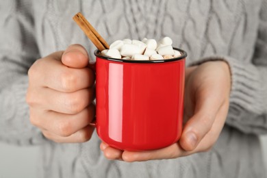 Photo of Woman holding cup of delicious hot chocolate with marshmallows and cinnamon stick, closeup