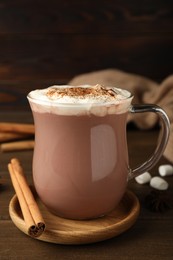 Photo of Glass cup of hot cocoa with whipped cream and aromatic cinnamon on wooden table