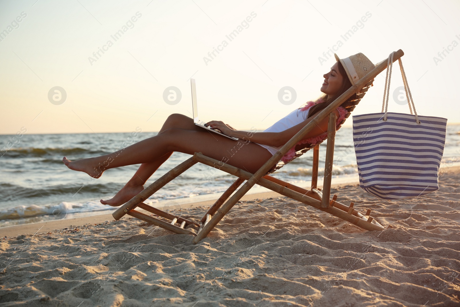 Photo of Young woman with laptop in deck chair on beach