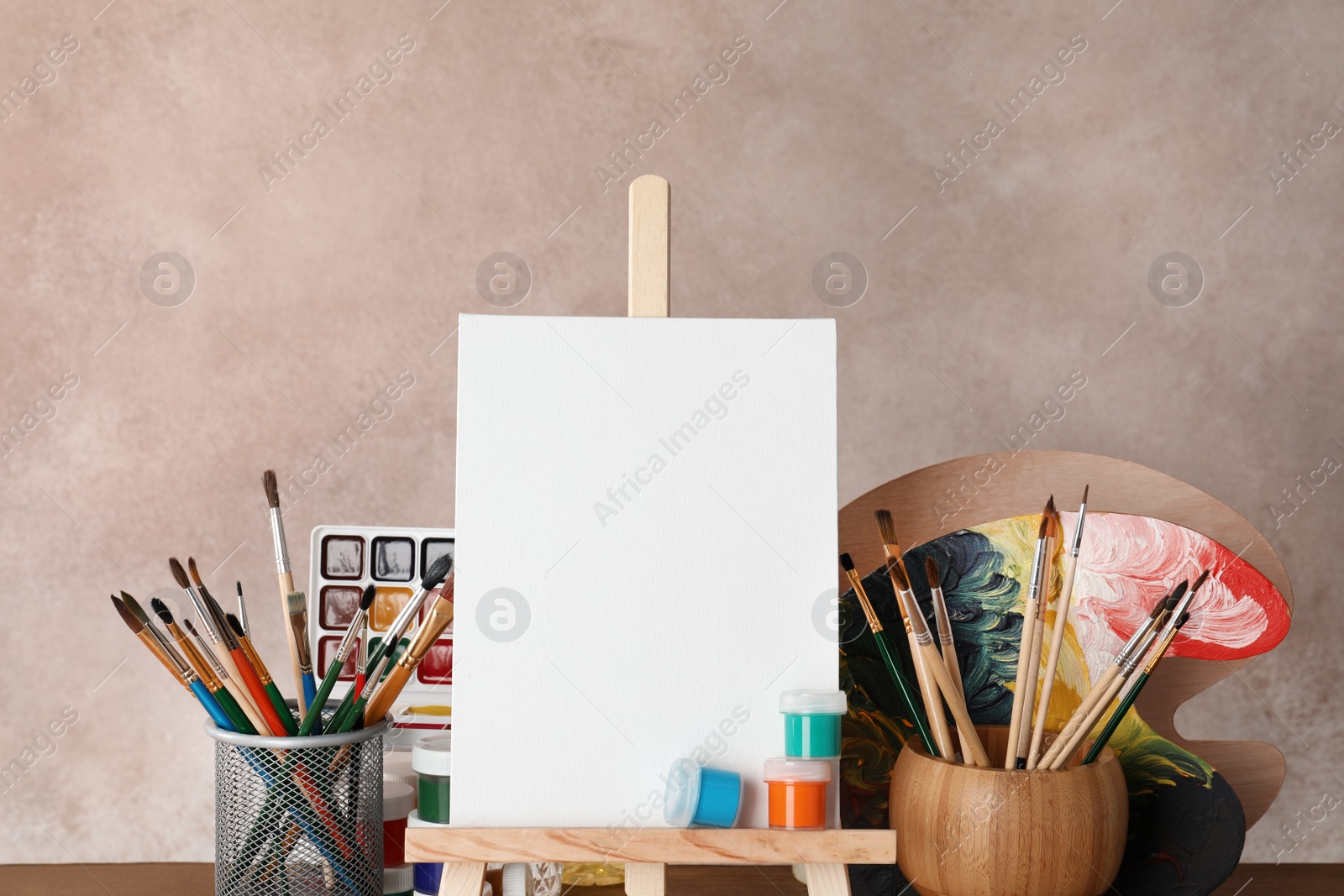 Photo of Wooden easel with blank canvas board and painting tools for children on color background