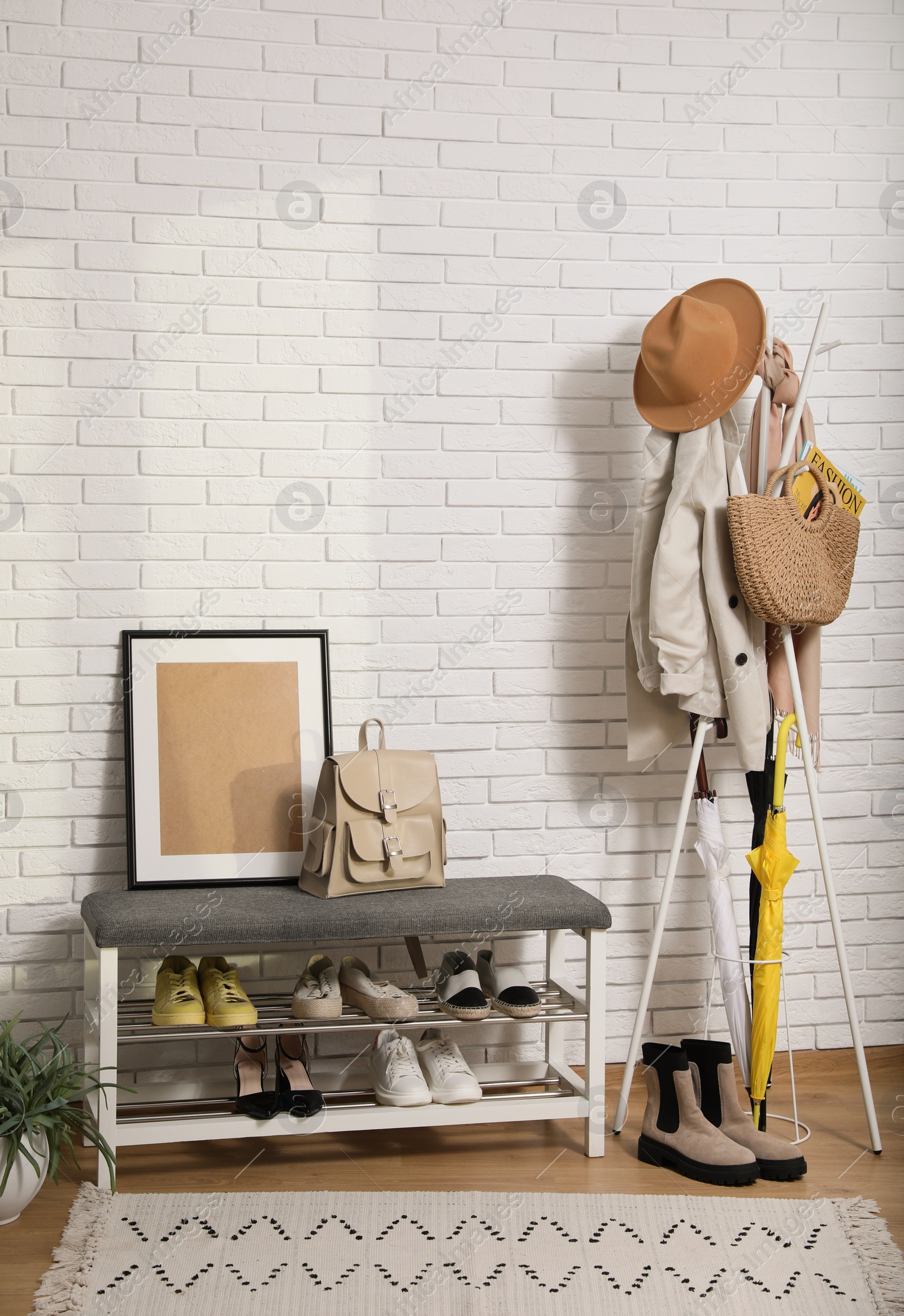 Photo of Stylish hallway interior with coat rack and shoe storage bench near white brick wall