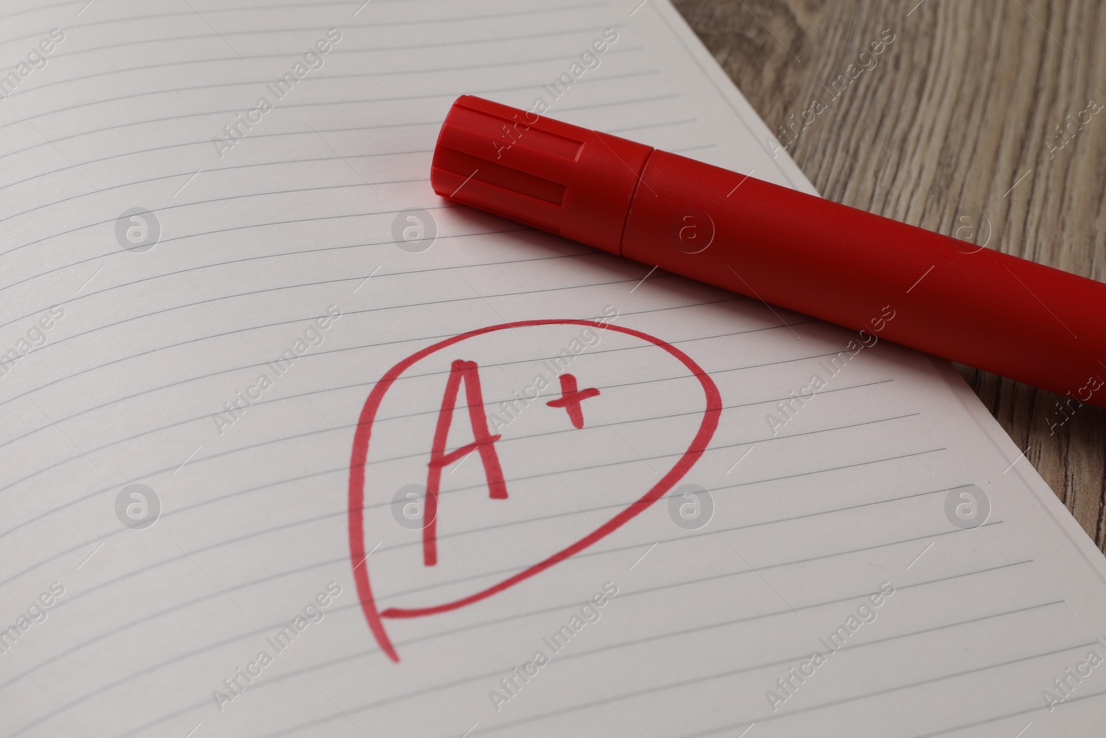 Photo of School grade. Red letter A with plus symbol on notebook paper and marker on table, closeup