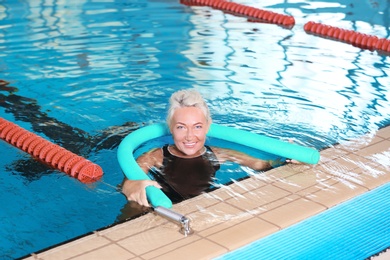 Photo of Sportive senior woman with swimming noodle in indoor pool